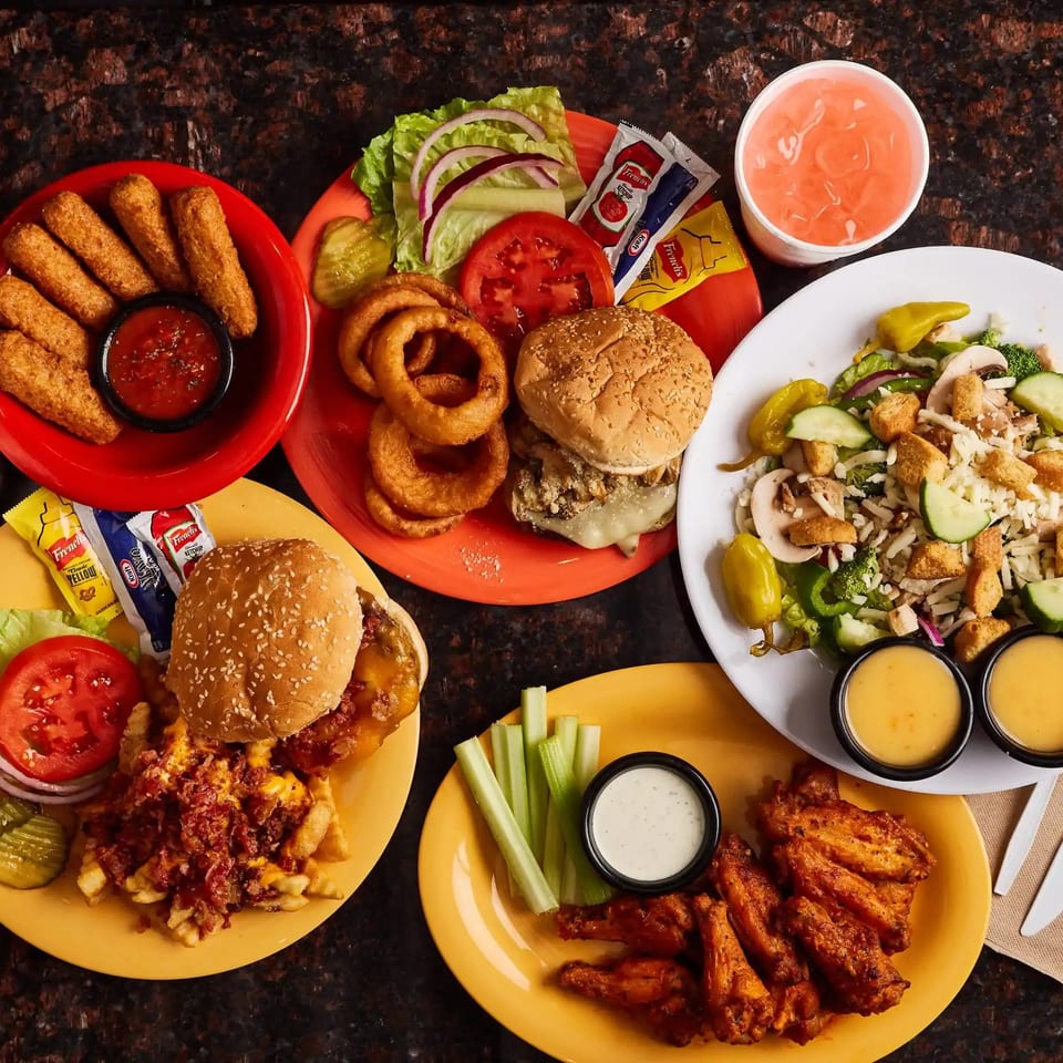 Wingz spread with burgers, mozzarella sticks, onion rings, salad, wings, and a pink drink.